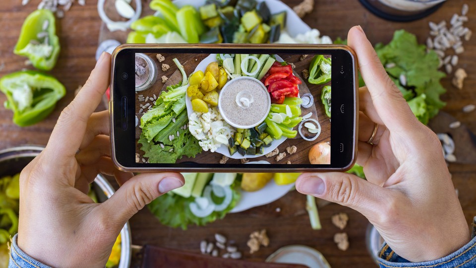 A person uses a smartphone to photograph a platter of vegetables and vegan mayonnaise.