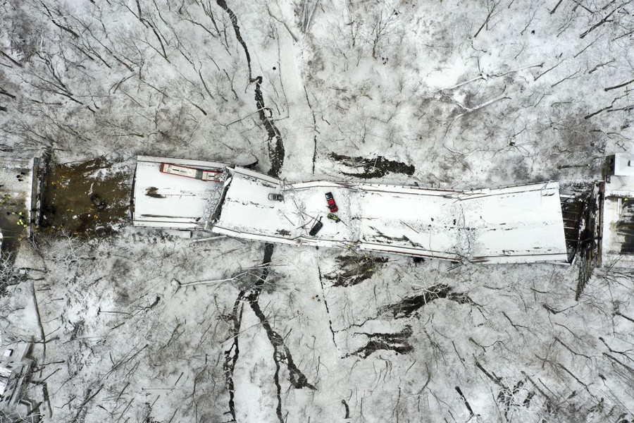 An aerial view of a collapsed road bridge and ravine, covered in a light coating of snow.