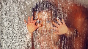 The blurry outline of a parent holding a child with their hands pressed to a glass pane covered in water droplets