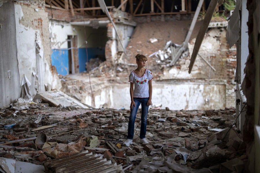 A child stands amid rubble in a destroyed classroom.