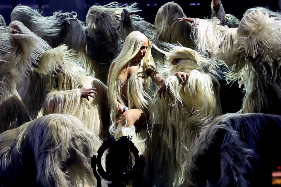 Performers wearing costumes covered in long strands of hair perform onstage.
