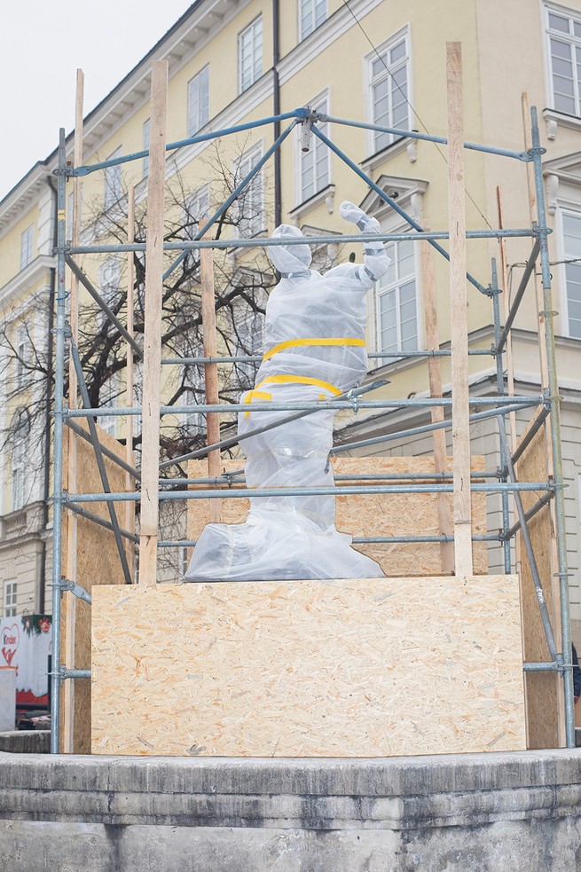 photo of outdoor sculpture wrapped in protective materials with metal cage and plywood surrounding it