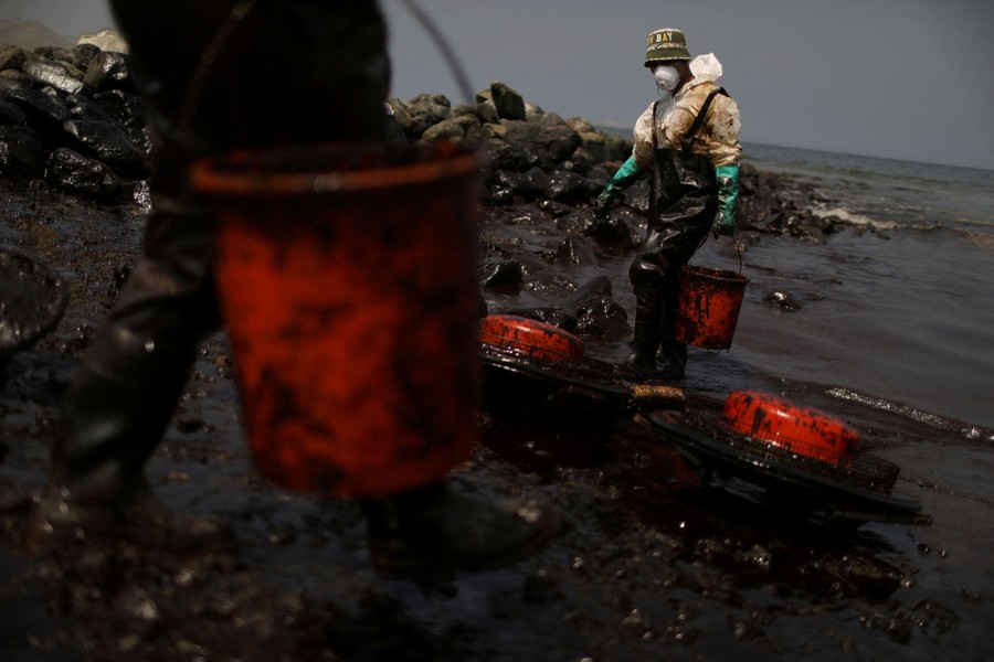Two workers carry buckets on an oil-fouled beach.