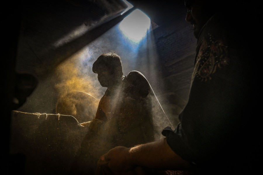 People work in a dark and dusty space lit by a shaft of sunlight.