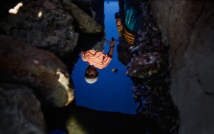 A reflection of two children in a small body of water, surrounded by rocks.