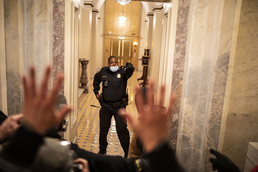 A single police officer in a hallway gestures toward an oncoming crowd.