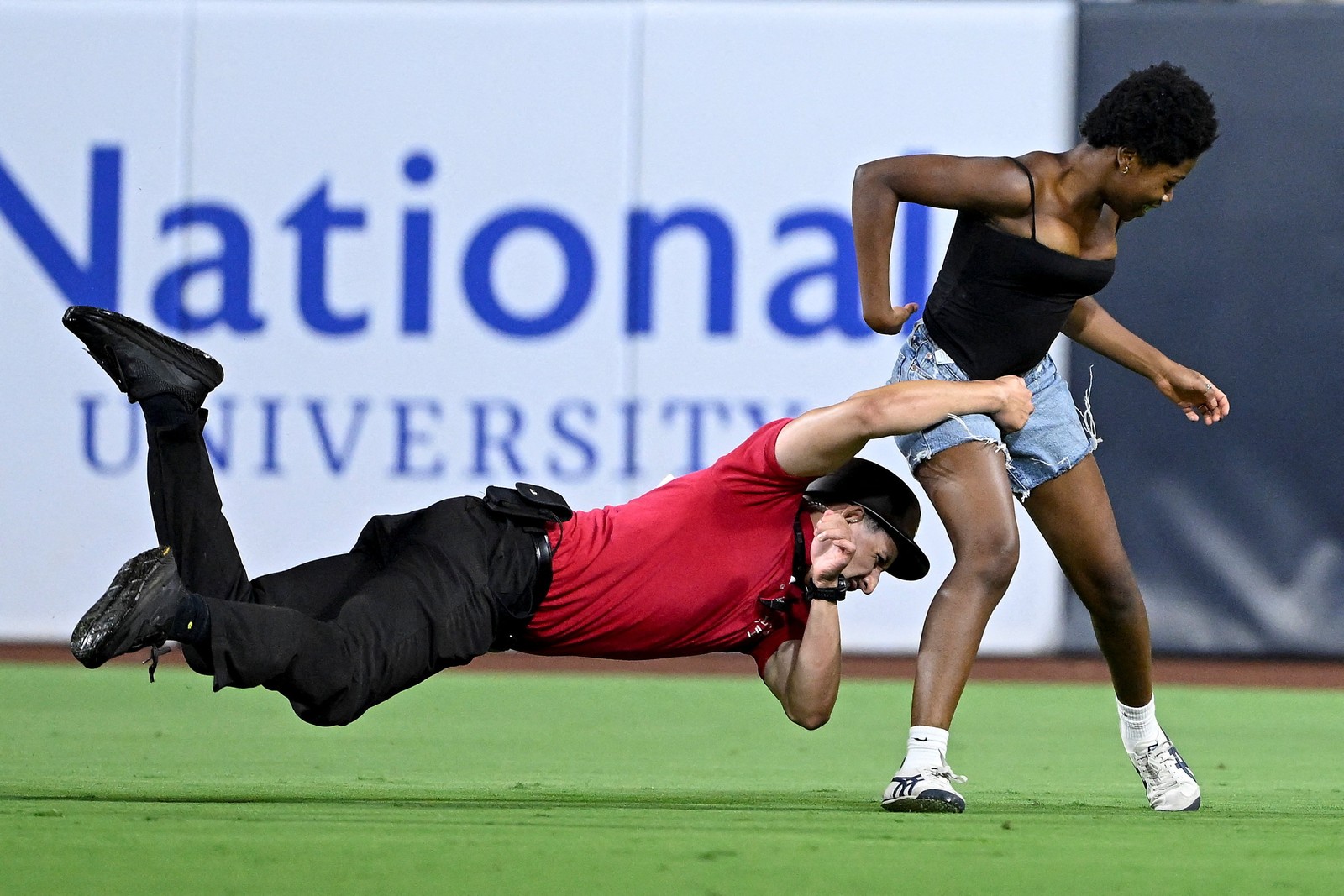 A security guard makes a flying tackle, trying to grab a fan who ran onto a sports field.