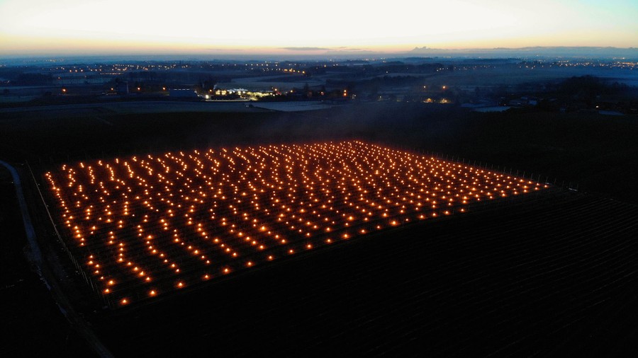 An aerial view of large candles burning among a fruit tree grove.