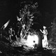 An older black-and-white photo of several men wearing broad-brimmed hats talking while gathered around a campfire at night
