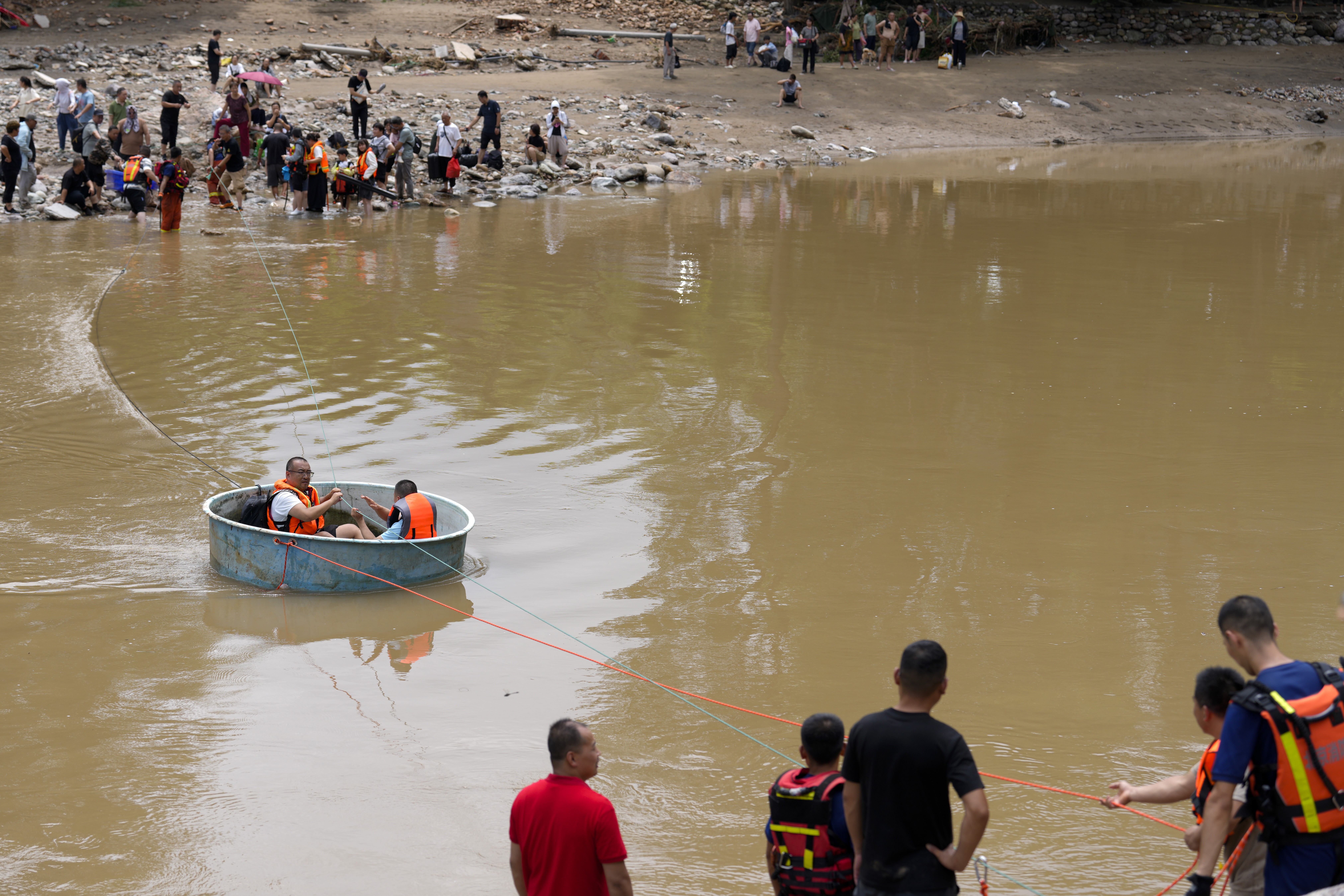 Rescuers pull on a rope, towing people across a flooded river in a round plastic basin.