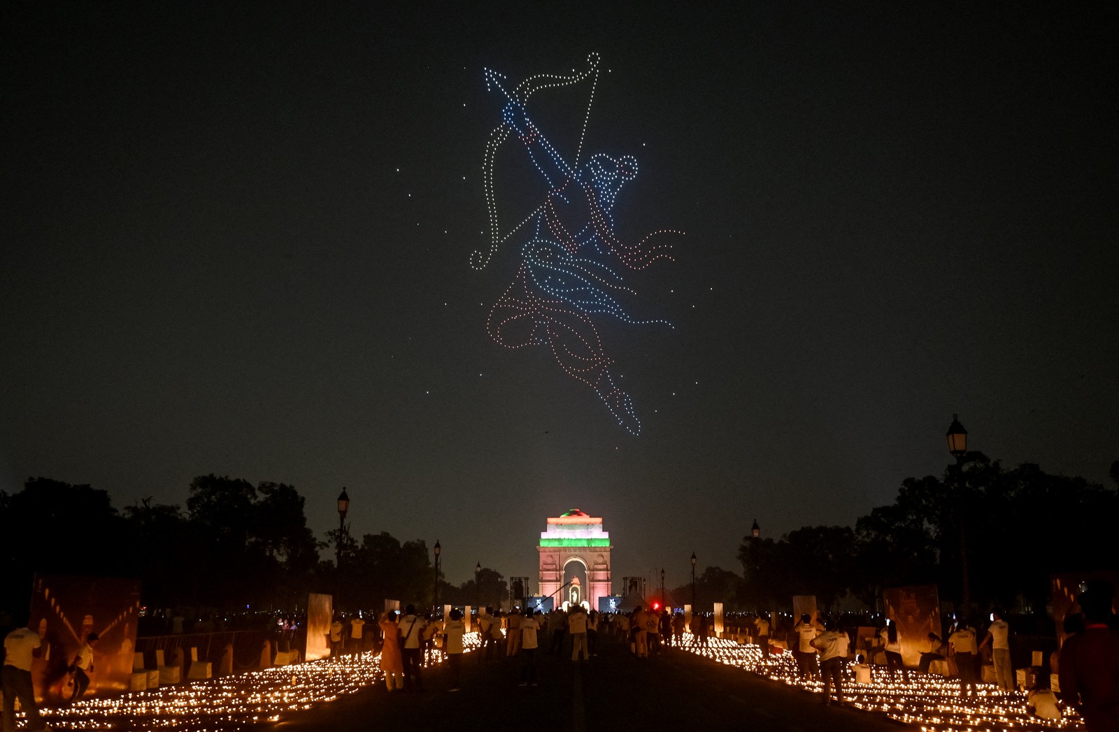Thousands of lit oil lamps, arranged on the ground beneath a drone light show depicting a mythical Hindu character with a bow and arrow.