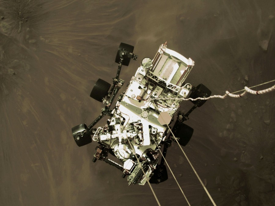 A top-down view of a Mars rover being lowered onto the surface of Mars