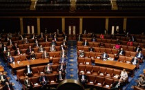 An overview shot of the House of Representatives, with members wearing suits or blazers and sitting scattered throughout the rows of desks