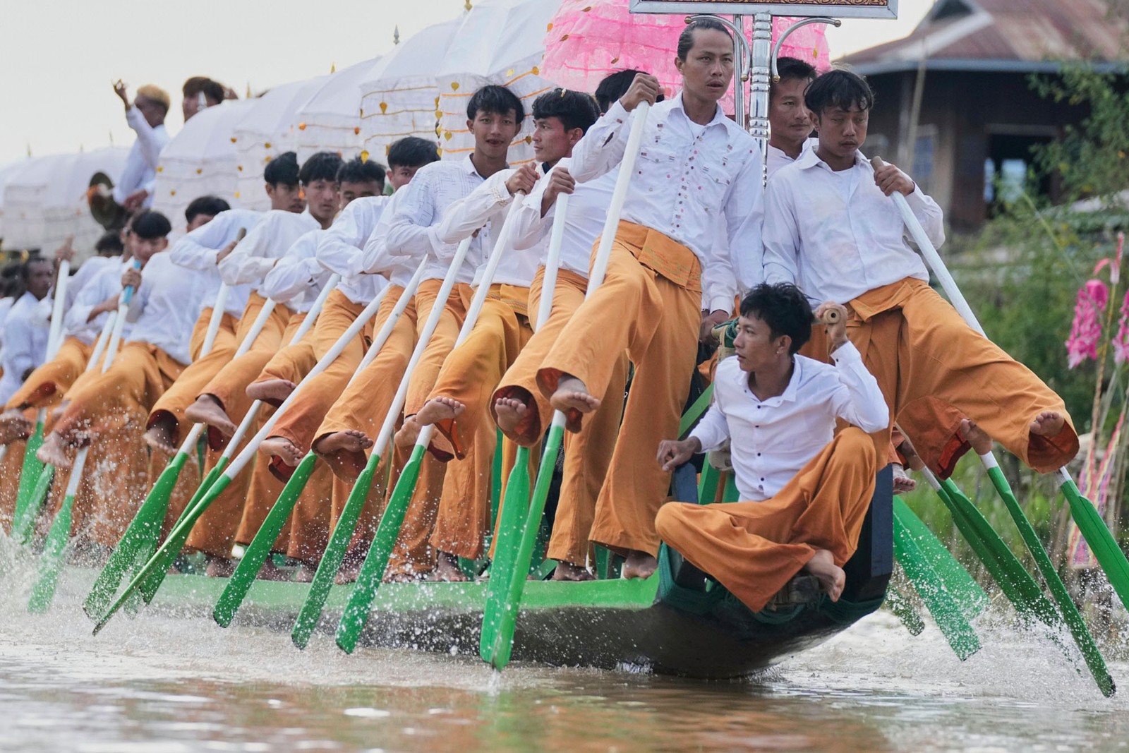 A crew of rowers use their legs to paddle a long boat during a festival.