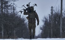 A soldier carries a drone on their shoulder while walking on a snow-covered road.