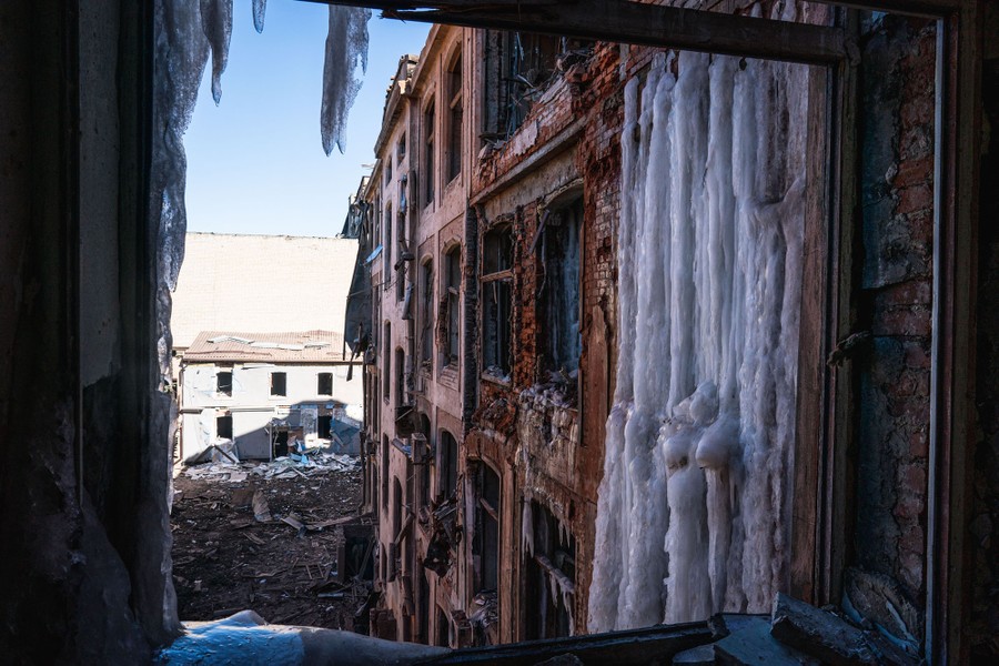 A view out the window of a damaged apartment building, with one of its exterior walls partially covered by ice.