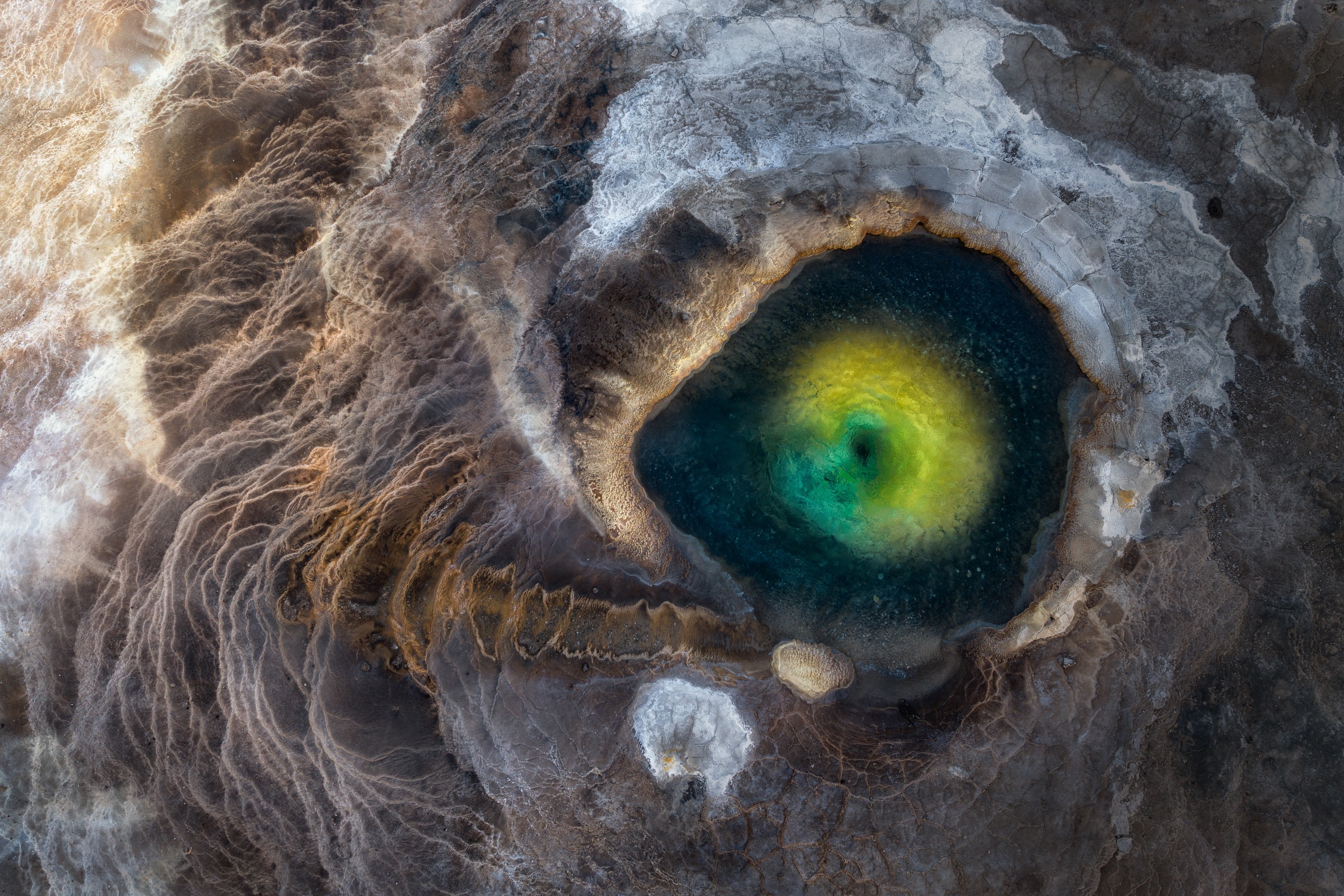 An aerial view of a colorful geothermal pool, looking like the eye of some fearsome creature.