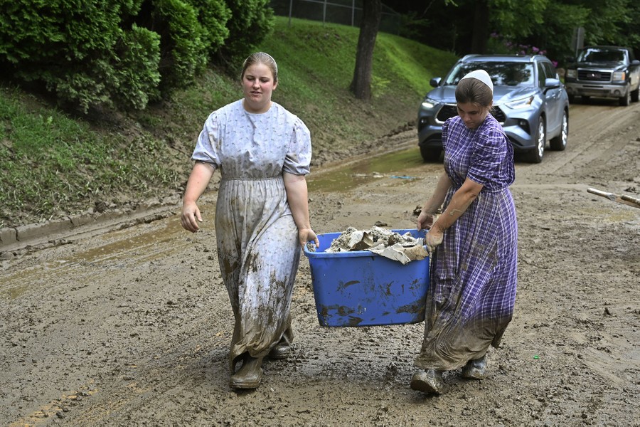 Two people work together to carry a tub full of debris on a muddy road.