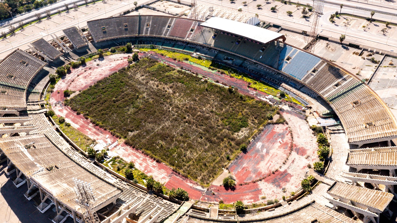 An aerial view of a closed soccer stadium, seen with an overgrown field