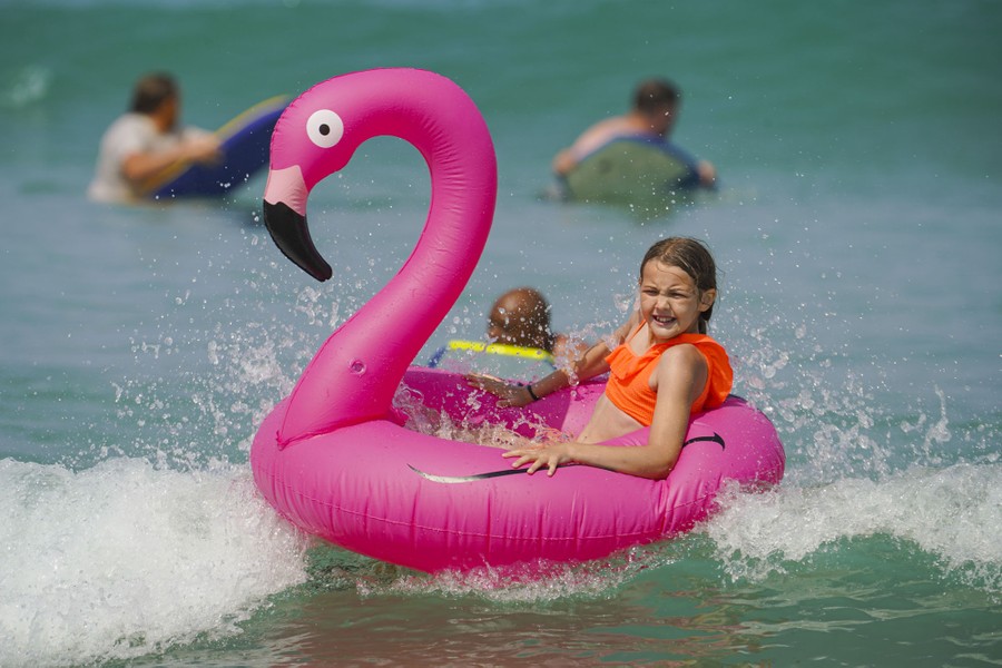 A young girl rides an inflatable flamingo in shallow waves.