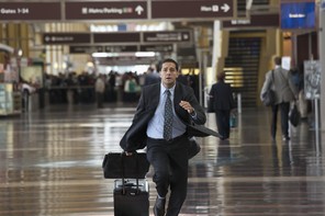 A man wearing a suit runs through the airport with his luggage