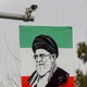Photo of a surveillance camera overlooking a banner featuring a portrait of Ali Khamenei overlaid on green, white, and red stripes resembling the Iranian flag.