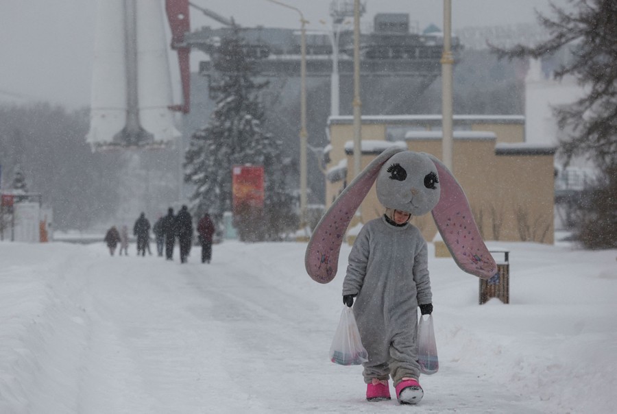 An entertainer in a large bunny costume walks in a street during a snowfall.