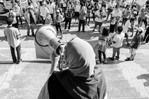 Picture showing an activist wearing a hijab holding a megaphone, speaking to a crowd of protesters holding signs. One of the signs reads: "Free Palestine."