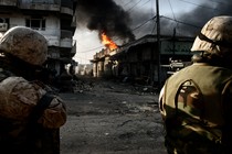 Soldiers shoot at a street that's burning.