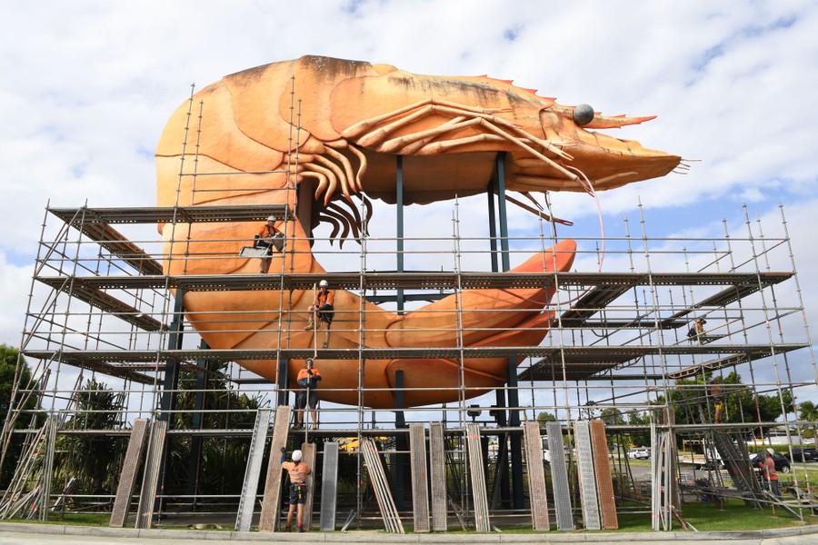 Workers install scaffolding around a huge statue of a prawn.
