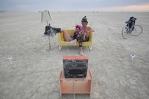 Two people sitting on a yellow sofa watching TV at Burning Man