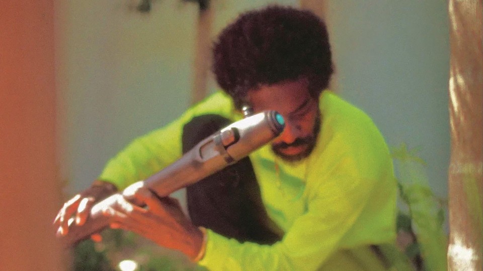 André 3000 crouching in a neon yellow-green shirt holding a flute