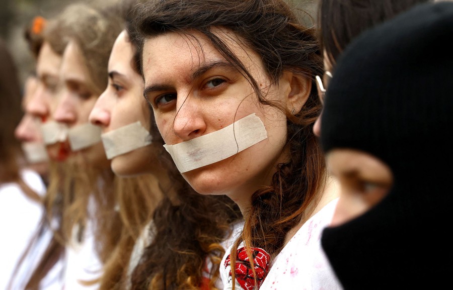 Several women are seen during a protest, with their mouths taped closed.