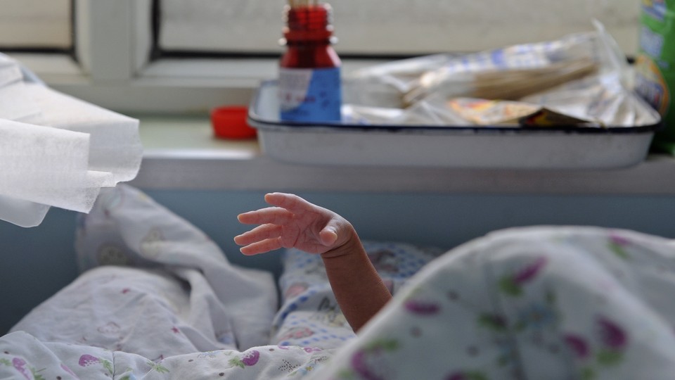 A baby stretches its hand from under a quilt in a hospital