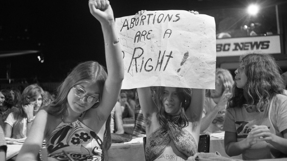 women holding up a protest sign that reads "abortions are a right!"