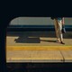Color photograph of a woman, half in shadow, standing on a train platform.