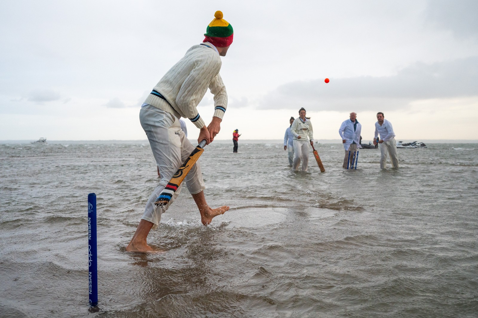 People play a game of cricket while standing in shallow water.