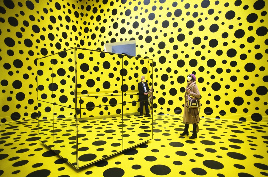 People walk through a large room that is painted bright yellow and covered in hundreds of black polka dots.