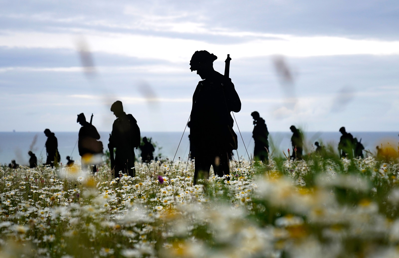 A memorial made of life-sized silhouette cutouts of soldiers standing in a field of flowers