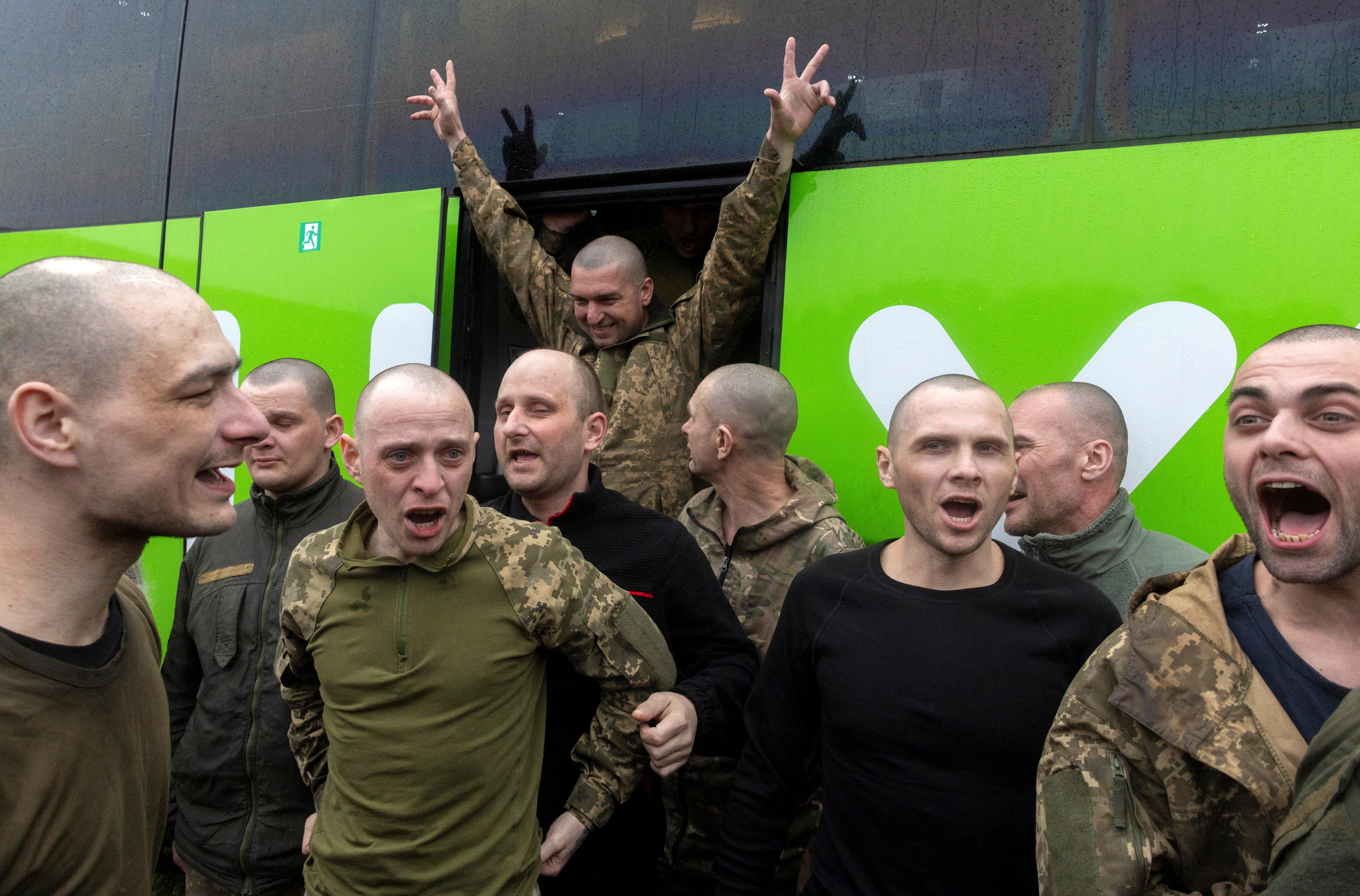 Ukrainian servicemen, recently-released war prisoners, react joyfully outside a bus after returning home.