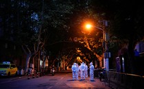 A half dozen people wearing protective gear stand in a street under a street lamp.