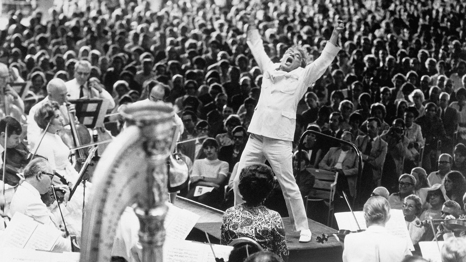 A black-and-white photograph of Leonard Bernstein conducting an orchestra in front of a crowd