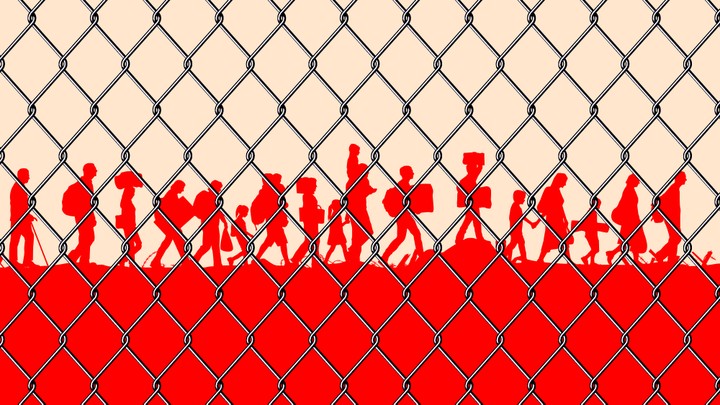 Silhouettes of migrants behind a chain-link fence.