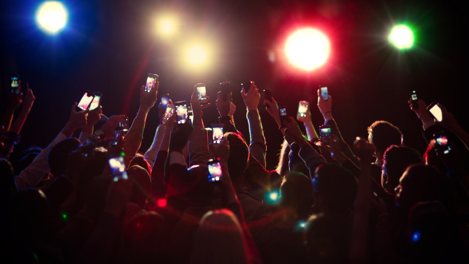 People in the crowd at an event hold their phones in the air