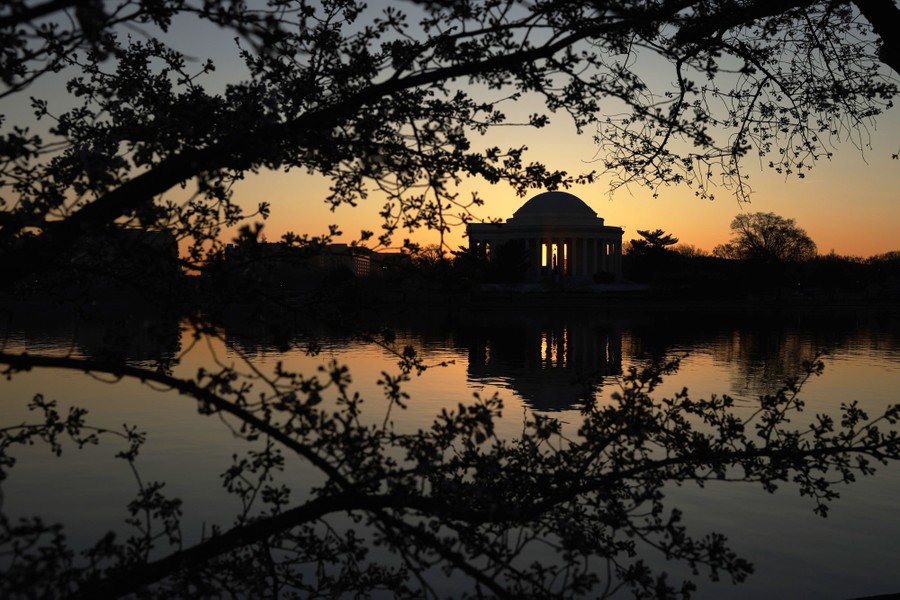 The sun rises behind the Thomas Jefferson Memorial, reflected in a pool.