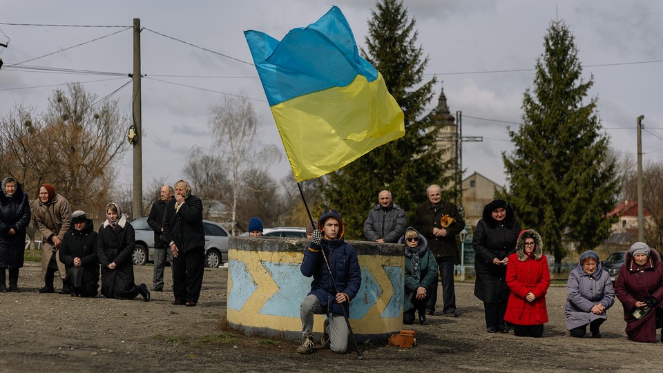 Ukrainians kneeling in a show of mourning, as one person holds a Ukrainian flag.