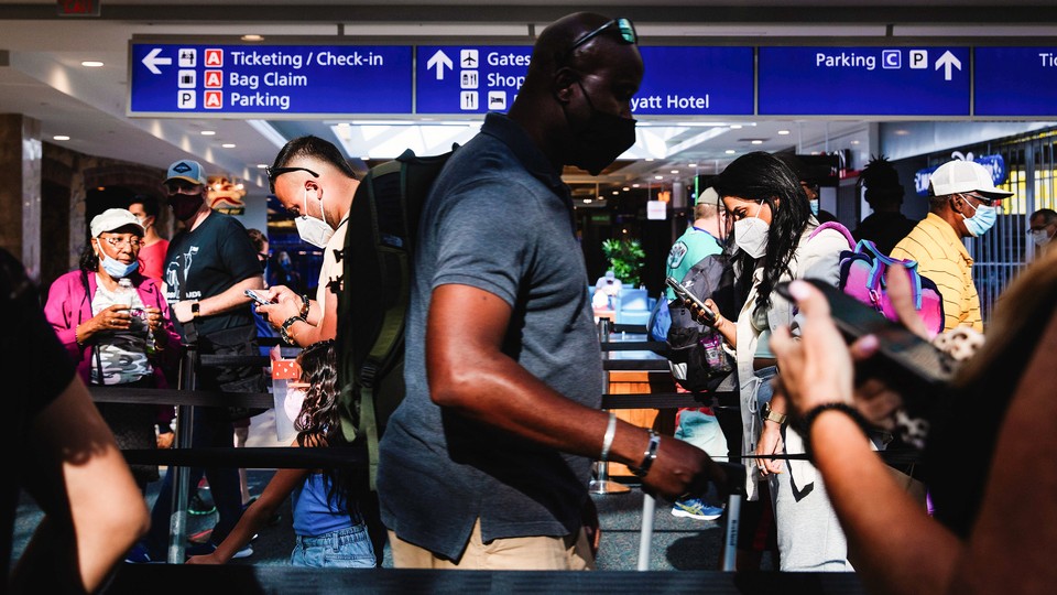 A man with a face mask stands in line at a crowded airport.