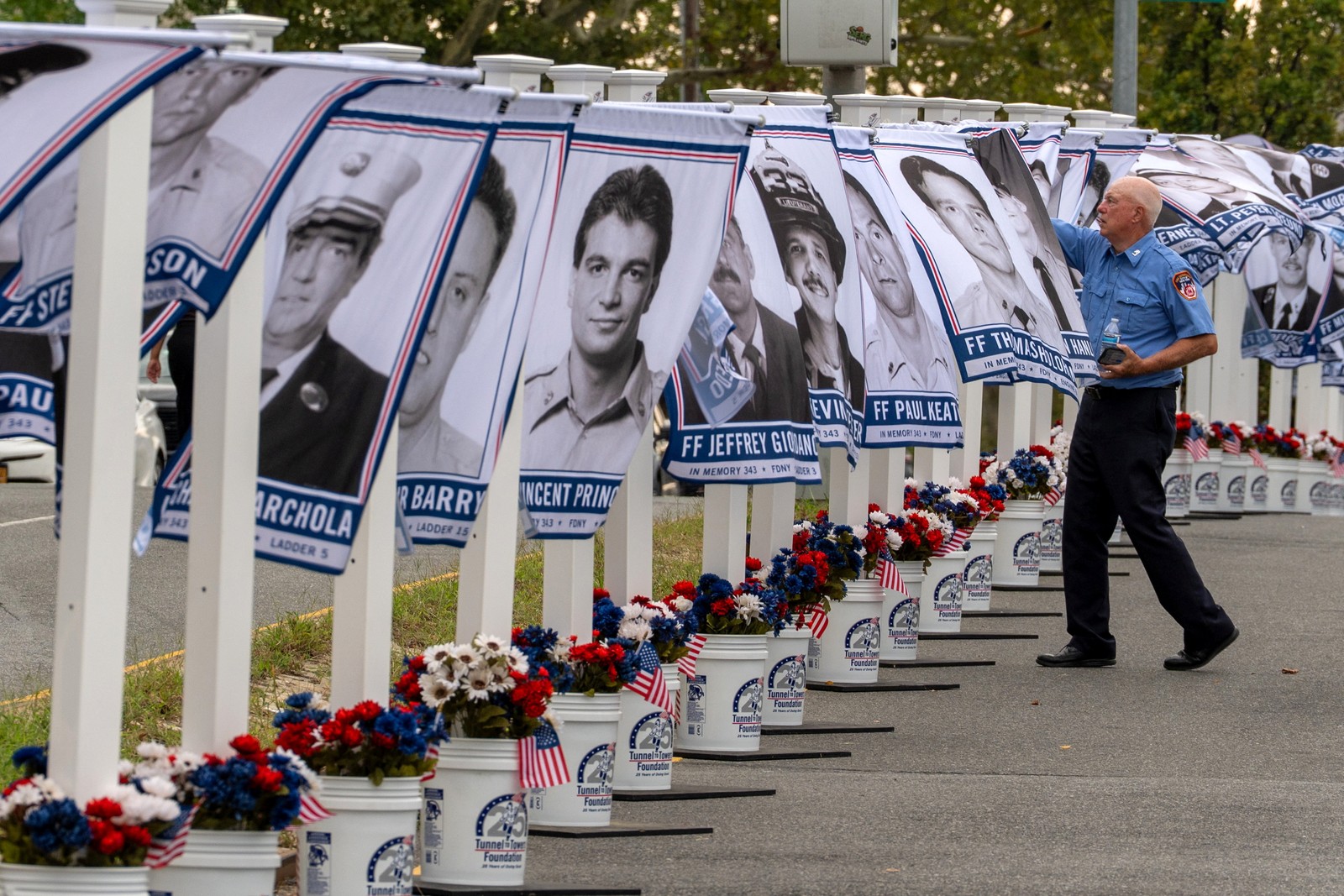 A firefighter fixes a windblown photo of a first responder on a flag hanging from a pole, among a display of many others, at a memorial.