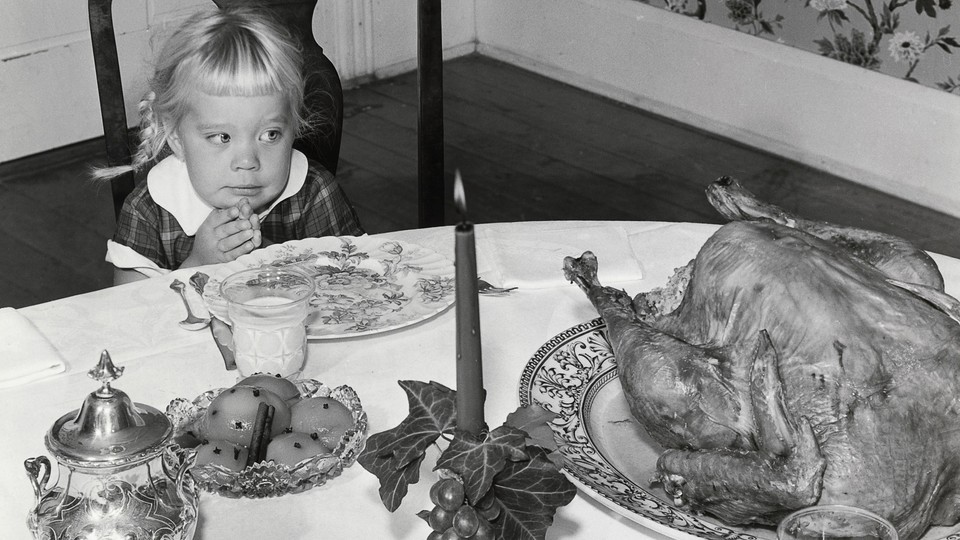 A young girl sits before a large roast turkey.