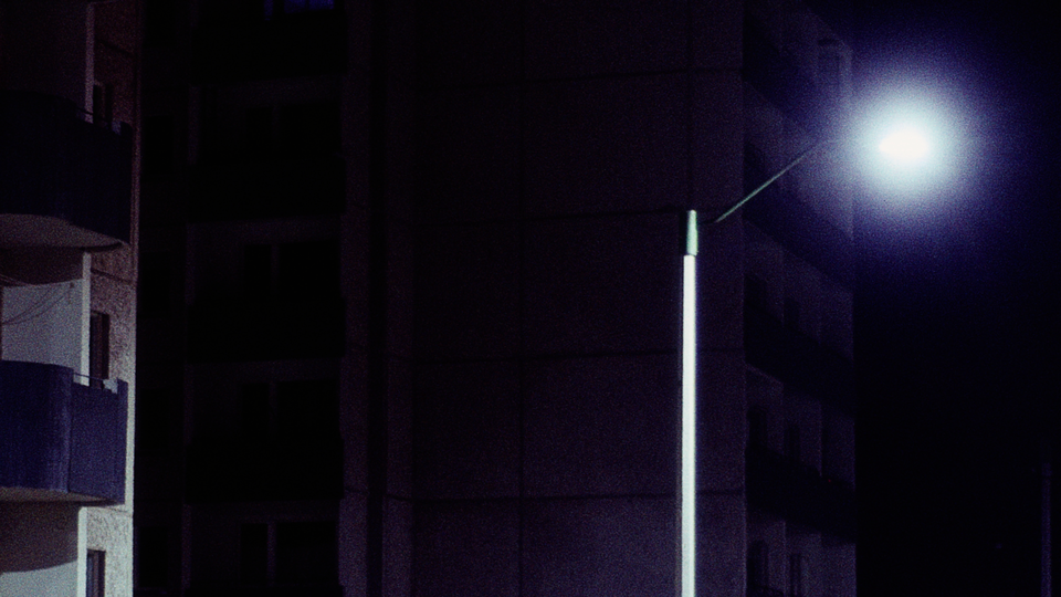 night photo of edge of building with balcony next to bright streetlight with pitch-black background